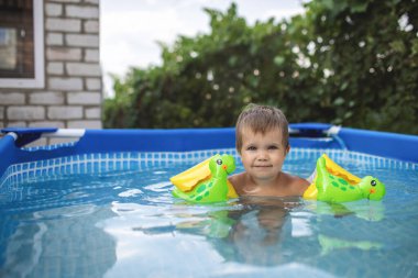 Üst kollu çocuk bahçedeki havuzda yüzüyor.