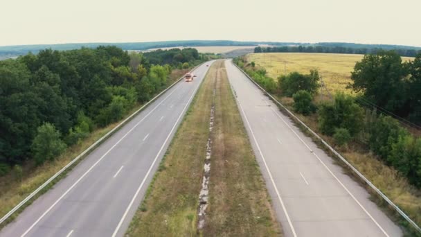 Carros dirigem em uma faixa de longa estrada que se estende entre árvores — Vídeo de Stock