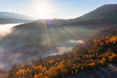 Pembe ve mor gökyüzünde gün batımı parlıyor. Dağlık kanyon manzarasını kaplayan kalın beyaz sis tabakasının üzerinde.