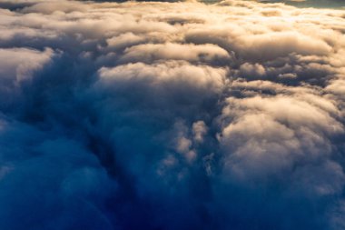 Kalın kabarık bulutların üzerindeki mavi gökyüzü parlak turuncu renkli gündoğumu ve manzara manzarasının altındaki dağ zirveleri.