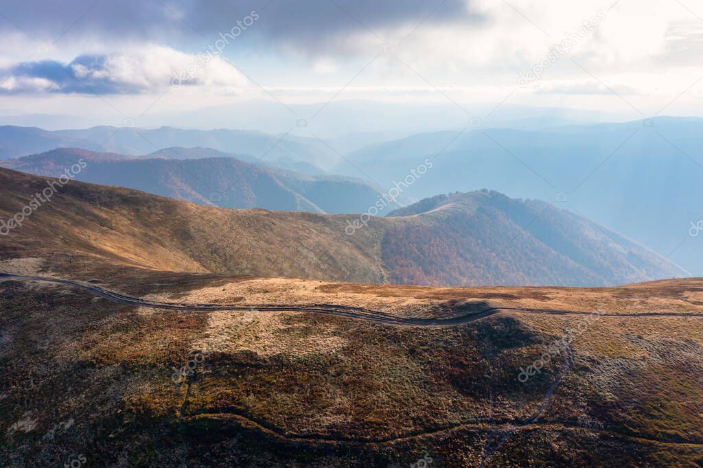 Long narrow pathways running along high mountain ridge under white fluffy clouds floating on blue sky on sunny day aerial view