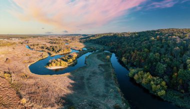 Yeşil çayırlar ve uzun, dar nehirler arasında uzanan ve mavi bulutsuz gökyüzü manzarasının altında koyu su bulunan köy yolu.