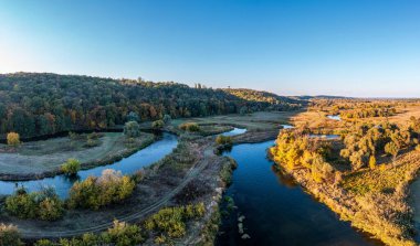 Yeşil çayırlar ve uzun, dar nehirler arasında uzanan ve mavi bulutsuz gökyüzü manzarasının altında koyu su bulunan köy yolu.