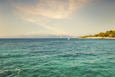 Anchored motorboat on calm water surface against Corfu island with buildings and mountains under blue sky with white puffy clouds