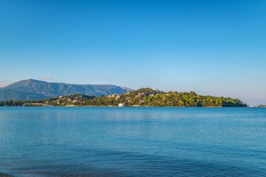 Blue sea against landscape of hilly Corfu island with buildings surrounded by forests against high mountain panorama view