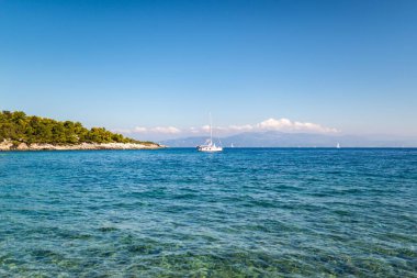 High rocky hilly island with forest on top near shore of Corfu in Greece with clear turquoise water under blue cloudless sky panorama view
