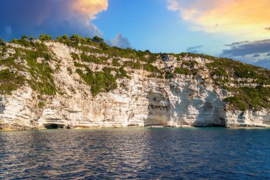 Light-colored layered rock creating cave on beach of Corfu island in Greece with clear turquoise water under blue cloudless sky