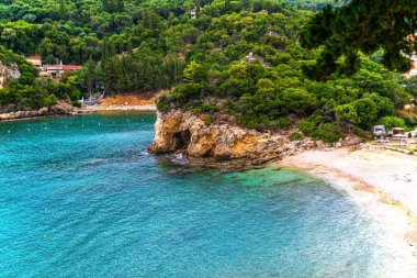 Green hills with rocky steep slopes and mountains surround hotel resort on sea bay beach under blue cloudy sky on Corfu island panorama view