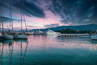 Yachts moored to pier under dark stormy clouds at sunset