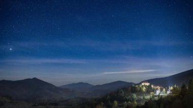 Yıldızlı gökyüzü, şehrin üzerinde süzülen beyaz bulutlarla dağlık bölgede