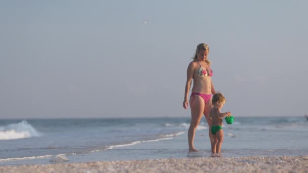 Anne oğluyla deniz kıyısında yürüyor yaz güneşinin altında deniz kabuğu topluyor. — Stok video