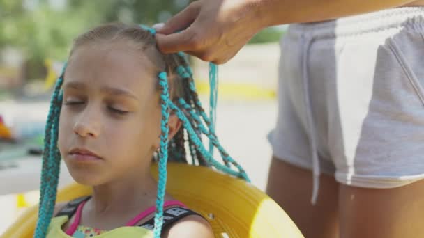 Una chica de traje teje trenzas africanas en su cabello en un día soleado — Vídeo de stock