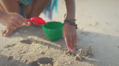 Yazlık kostümü içinde Afrika örgülü bir kız deniz kenarında deniz kabuklarıyla güneşli günbatımında dalgalarla sahilde oynuyor.