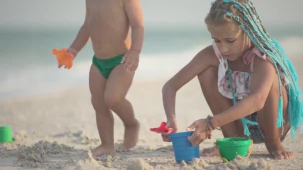 Äldre syster leker med yngre bror på grund nära stranden på sommarsemester — Stockvideo