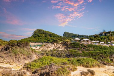 High hills with rocky slopes covered with dense forests around hotel resort under blue sky with orange-colored clouds at sunset panorama view