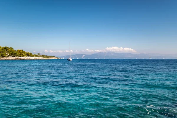 High rocky hilly island with forest on top near shore of Corfu in Greece with clear turquoise water under blue cloudless sky panorama view
