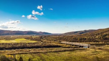 Dağlık arazide renkli ağaçlarla dolu bir nehir üzerindeki demiryolu köprüsü.