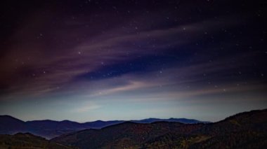 Sonbaharda dağların üzerinde pembe bulutlar olan gece yıldızlı gökyüzü
