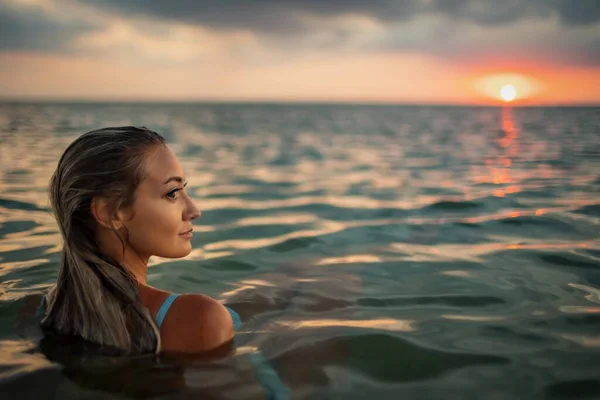 Una chica con hermosos rasgos faciales mira a una distancia desconocida mientras está sentada en el estuario —  Fotos de Stock