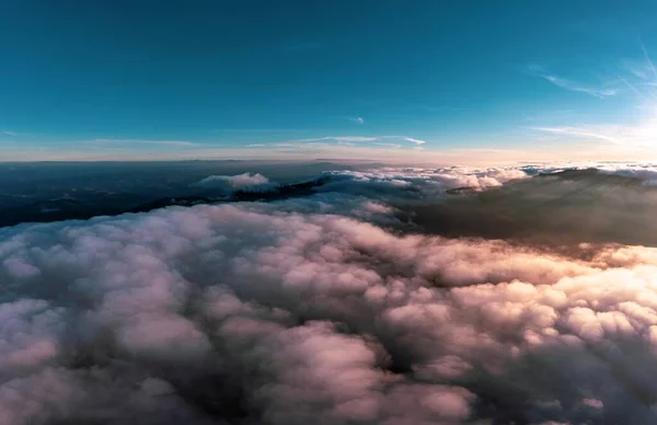 白いふわふわの雲の厚い層の上の青い空 パノラマビューの下に山の峰がある明るいオレンジ色の日の出 — ストック写真