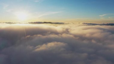 Güneş, gün doğumunda beyaz kabarık bulutların üzerinde parlıyor.