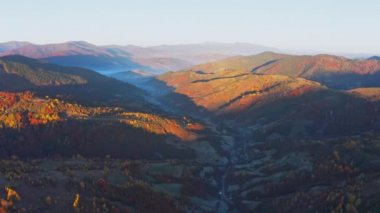 Gölgeli dağ vadisi, gün batımında evler ve ormanlar.