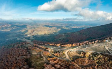 Sonbahar günü mavi gökyüzünde süzülen beyaz bulutların altında tepe boyunca uzanan dağ sırtı ve kayak pistlerine giden yol.