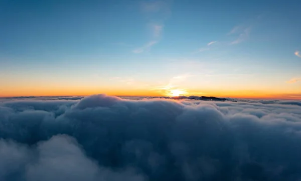 白いふわふわの雲の厚い層の上の青い空 パノラマビューの下に山の峰がある明るいオレンジ色の日の出 — ストック写真