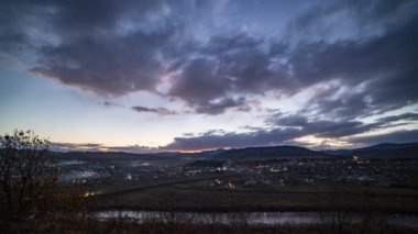 Gün batımında karanlık gökyüzünün altında küçük kasaba ışıkları yakar.