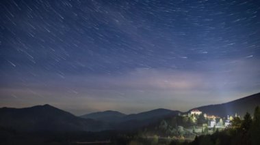 Yıldızlı gökyüzü, şehrin üzerinde süzülen beyaz bulutlarla dağlık bölgede