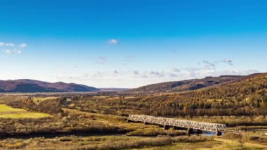 Dağlık arazide renkli ağaçlarla dolu bir nehir üzerindeki demiryolu köprüsü.