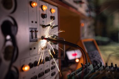Parlak, tehlikeli elektronik kıvılcımlar, karmaşık teknolojik ekipman üzerindeki güvenli olmayan kısa devreden hızlı ve keskin bir şekilde yayılıyor. Elektrikli aletlerle dolu karanlık bir odada.