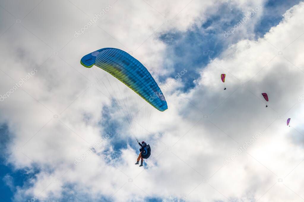 People try paragliding adventure sports flying with colorful parachutes against heavy white cumulus clouds on blue sky on autumn day