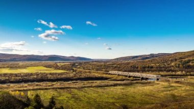 Dağlık arazide renkli ağaçlarla dolu bir nehir üzerindeki demiryolu köprüsü.