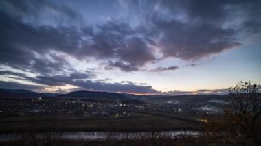 Gün batımında karanlık gökyüzünün altında küçük kasaba ışıkları yakar.