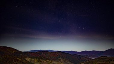 Sonbaharda dağların üzerinde pembe bulutlar olan gece yıldızlı gökyüzü
