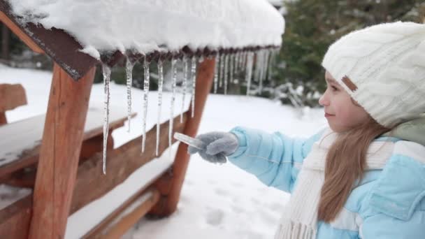 Dziewczyna sięgająca po sople z pokładu altanowego zimą. — Wideo stockowe