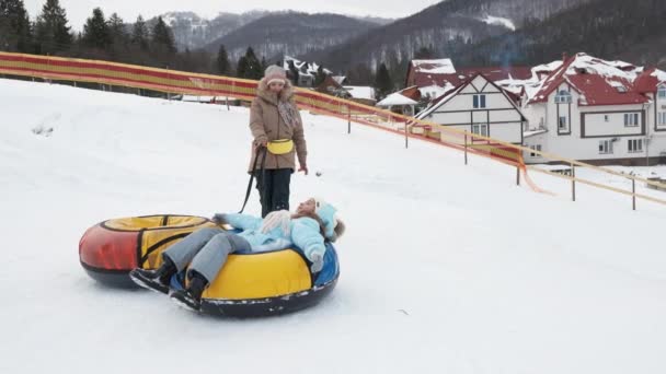 Girl helping her sister walk up snowy hill. — Stock Video