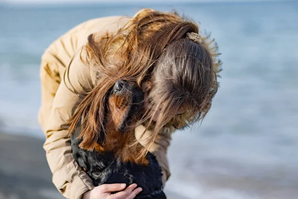 Дівчинка в куртці обіймає і дурний навколо з собака ротвейлера на пляжі біля моря — стокове фото