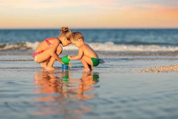 Kakak perempuan bermain dengan adik kandas dekat pantai pada liburan musim panas — Stok Foto