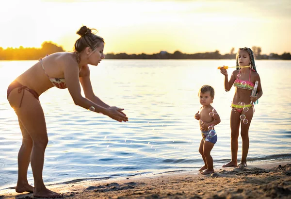 Frère et sœur jouent avec leur mère soufflant des bulles sur le lac — Photo