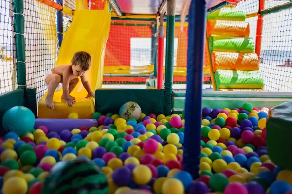 El niño juega en la sala de juegos y rueda por el tobogán en la piscina con pequeñas bolas — Foto de Stock