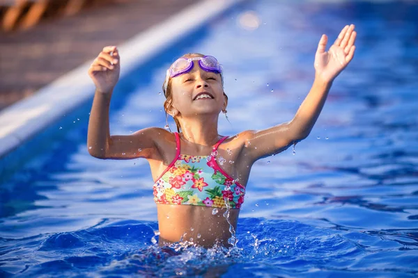 Una ragazza con gli occhiali da nuoto salta in una piscina con acqua limpida sullo sfondo di un caldo tramonto soleggiato estivo — Foto Stock