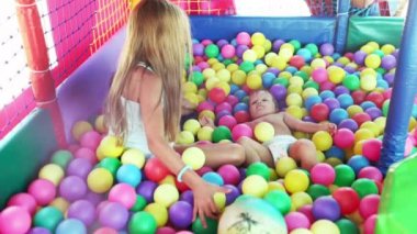 Ablası küçük erkek kardeşiyle oynuyor ve oyun odasında otururken ona küçük toplar atıyor.