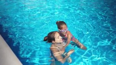 Parlak bikinili iki kız uzun zamandır beklenen bir tatilde mavi suyla birlikte havuzda oynuyorlar.