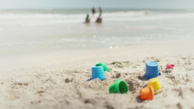 Birçok oyuncak, yaz güneşinin altında, deniz kıyısındaki sahilde yatıyor.