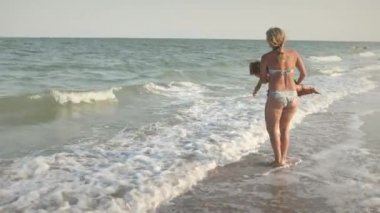 Anne oğlunu yaz tatilinde sıcak güneşin altında denize atıyor.