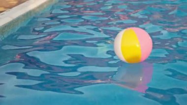 Parlak mayo giymiş bir kız, bir yaz akşamında havuzda şişme bir topla yüzer.