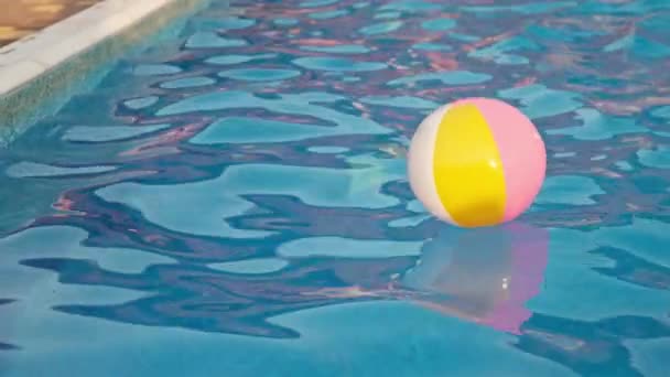 Una chica en un traje de baño brillante nada con una pelota inflable en una piscina con agua clara en una noche de verano — Vídeos de Stock