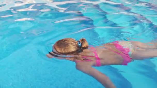 Uma menina em um maiô brilhante com óculos de natação mergulha em uma piscina com água transparente clara — Vídeo de Stock